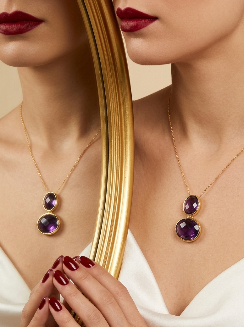 A close-up lifestyle shot of a model wearing a gold necklace with two stacked oval purple gemstones. The model is wearing a white satin top, dark red lipstick, and dark red nail polish, and is holding a large gold-framed mirror that reflects the necklace.