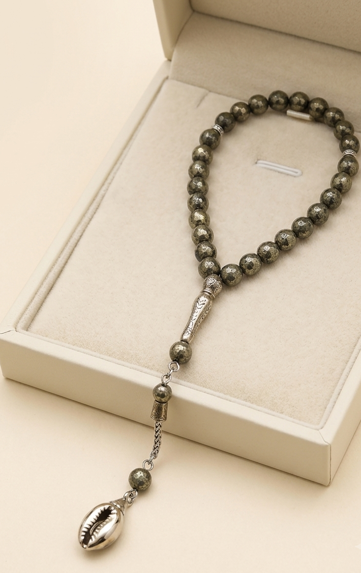 A beaded necklace with dark metallic beads and a silver-toned shell pendant, displayed inside an open cream-colored jewelry box.