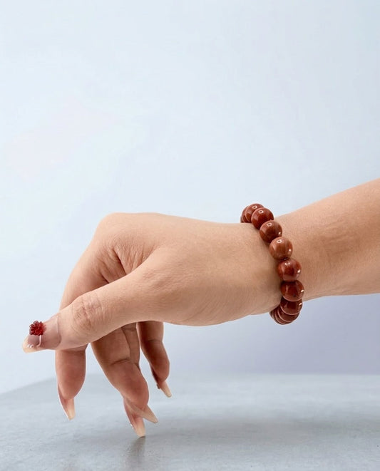 Hand wearing a red beaded bracelet on a light gray background