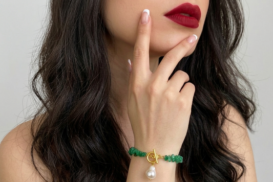 Woman wearing a green bracelet with a gold charm and pearl on a neutral background