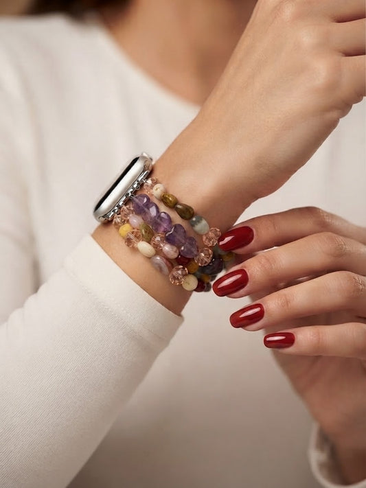 A close-up of a person wearing a multi-strand beaded bracelet with a silver-toned smartwatch, against a soft cream-colored background.