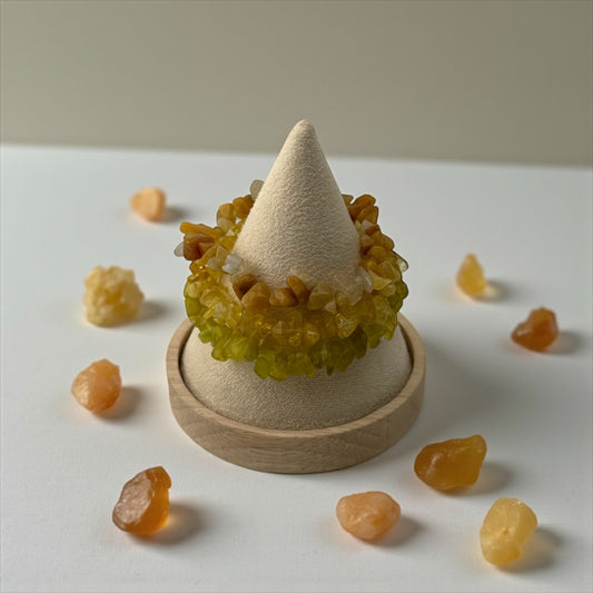 Decorative item with a cone-shaped top and wooden base surrounded by small orange stones on a white surface.