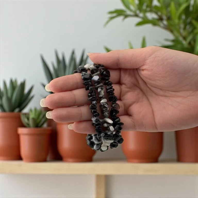 Hand holding a set of black and white beaded bracelets with potted plants in the background