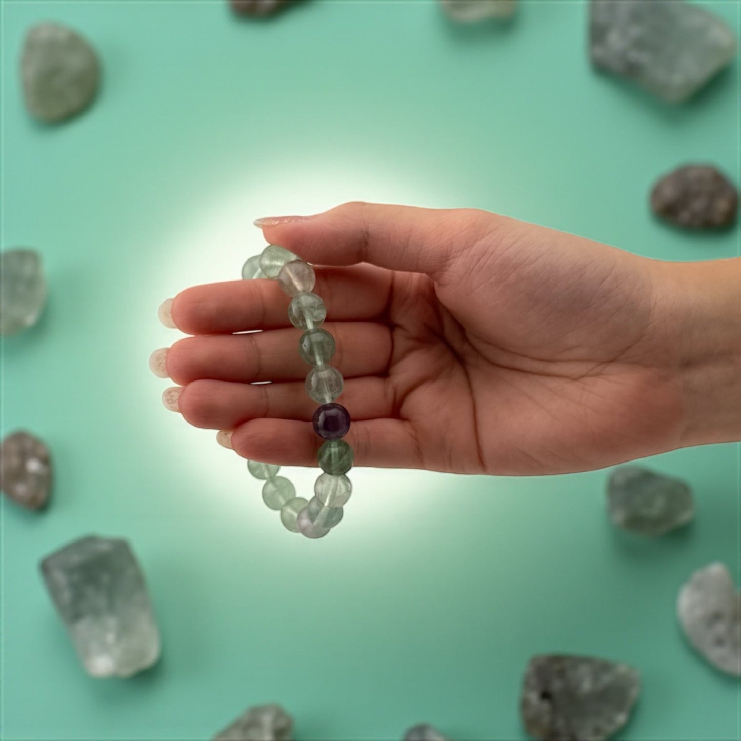 Hand holding a beaded bracelet with crystals on a teal background