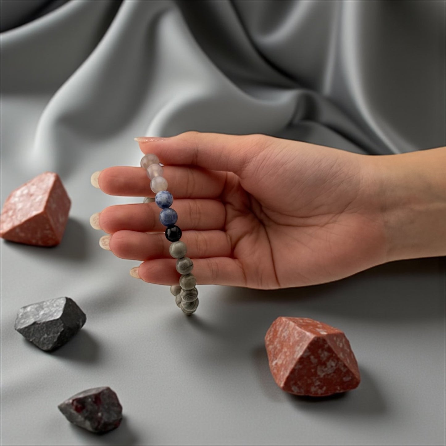 Hand holding a beaded bracelet with stones on a gray fabric background