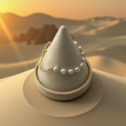Jewelry display with a gold ring and pearl necklace against a desert sunset background