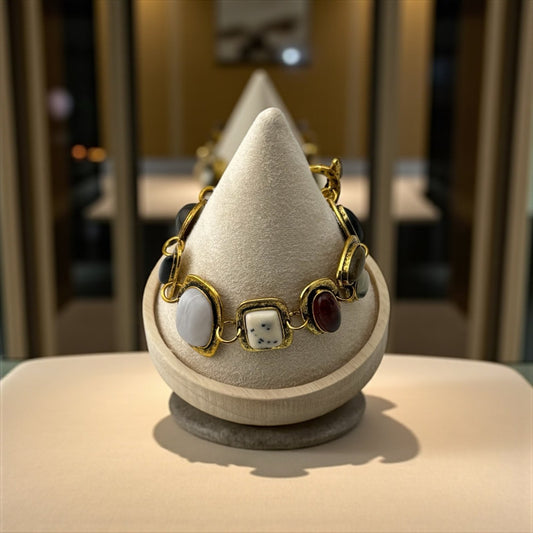 Bracelet with gold accents and gemstones on a textured stand with a blurred background