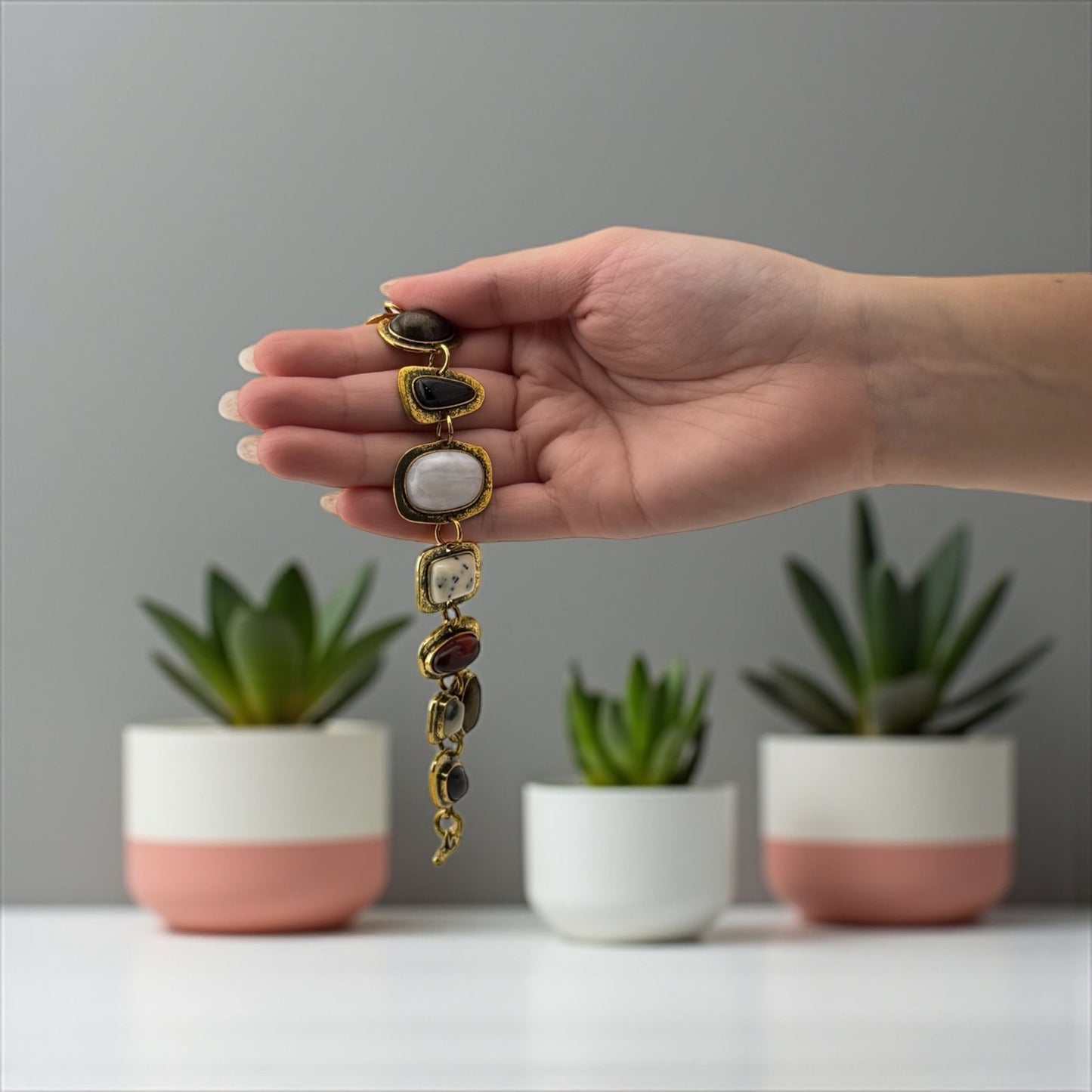 Hand holding a bracelet with three potted plants in the background
