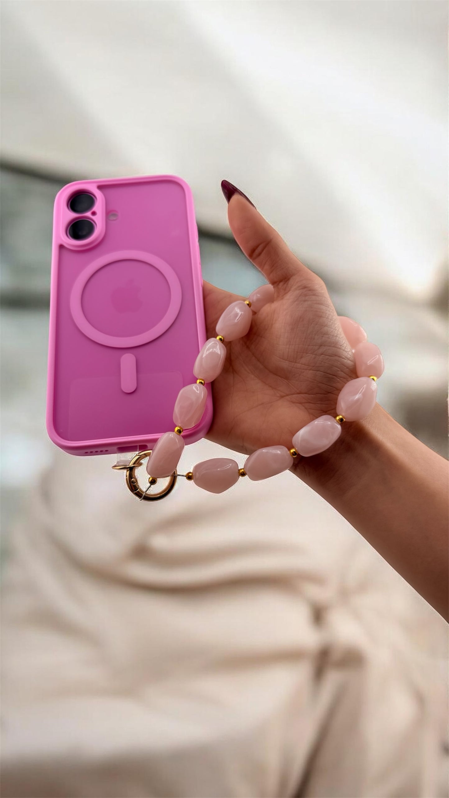 Hand holding a pink phone case with a matching necklace against a blurred background