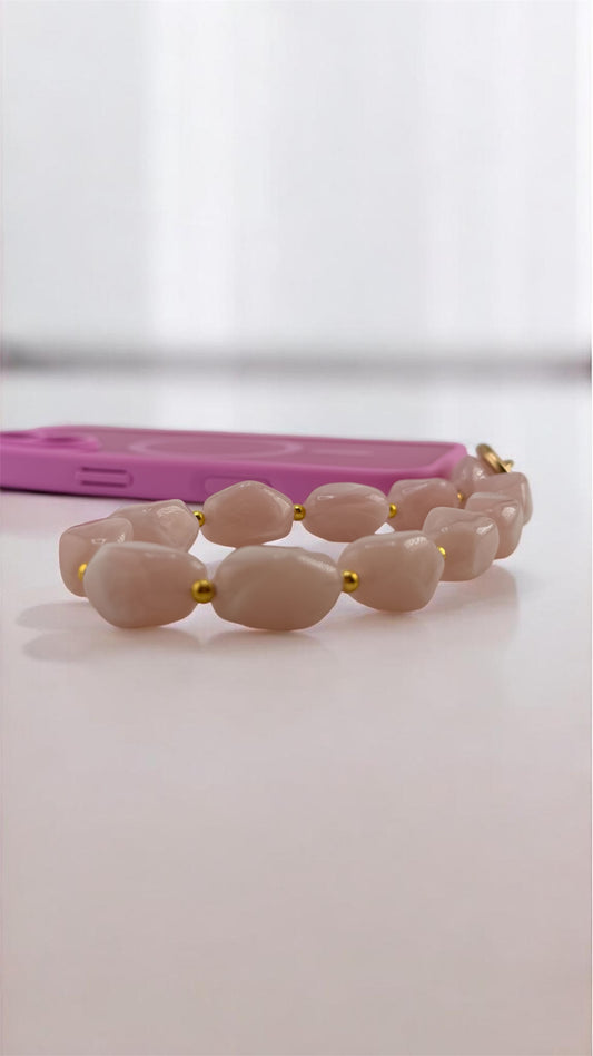 Beige beaded bracelet with gold accents on a white surface, pink phone case in the background