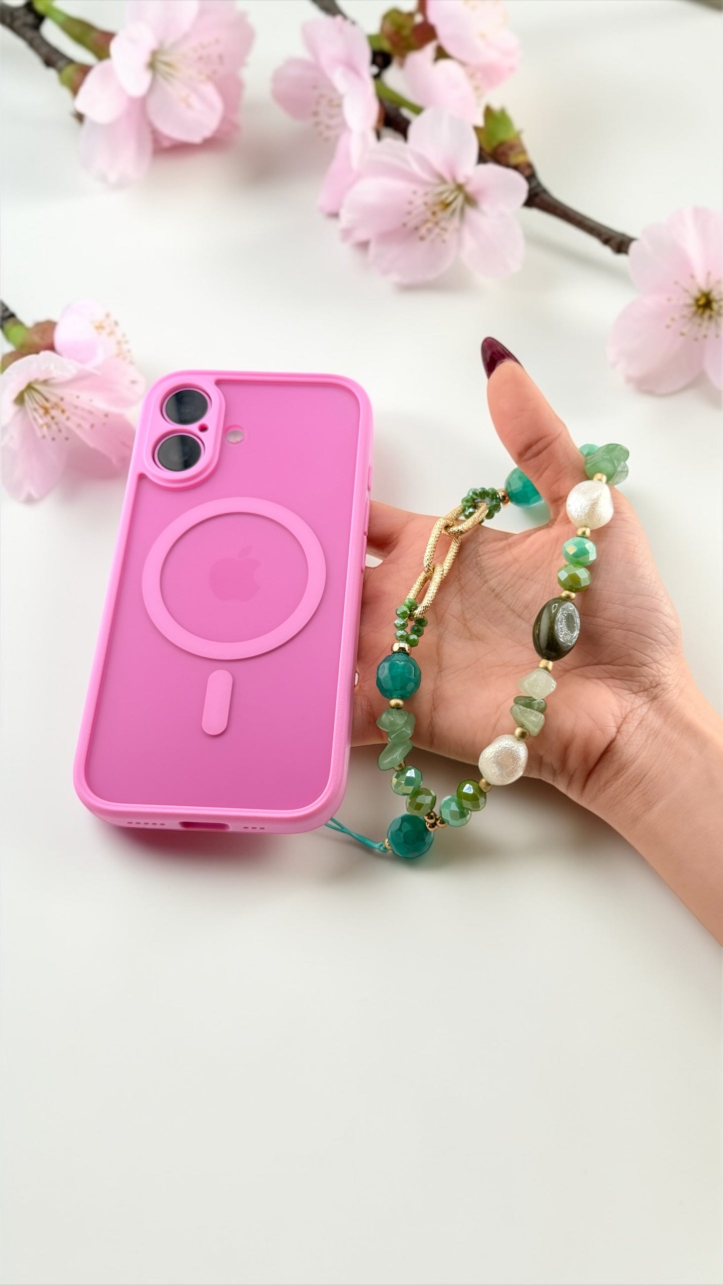 Pink phone case with a hand holding it, surrounded by cherry blossoms.