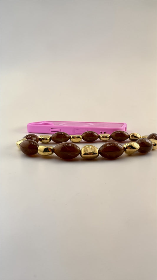 Brown beaded bracelet with gold accents on a pink case against a beige background
