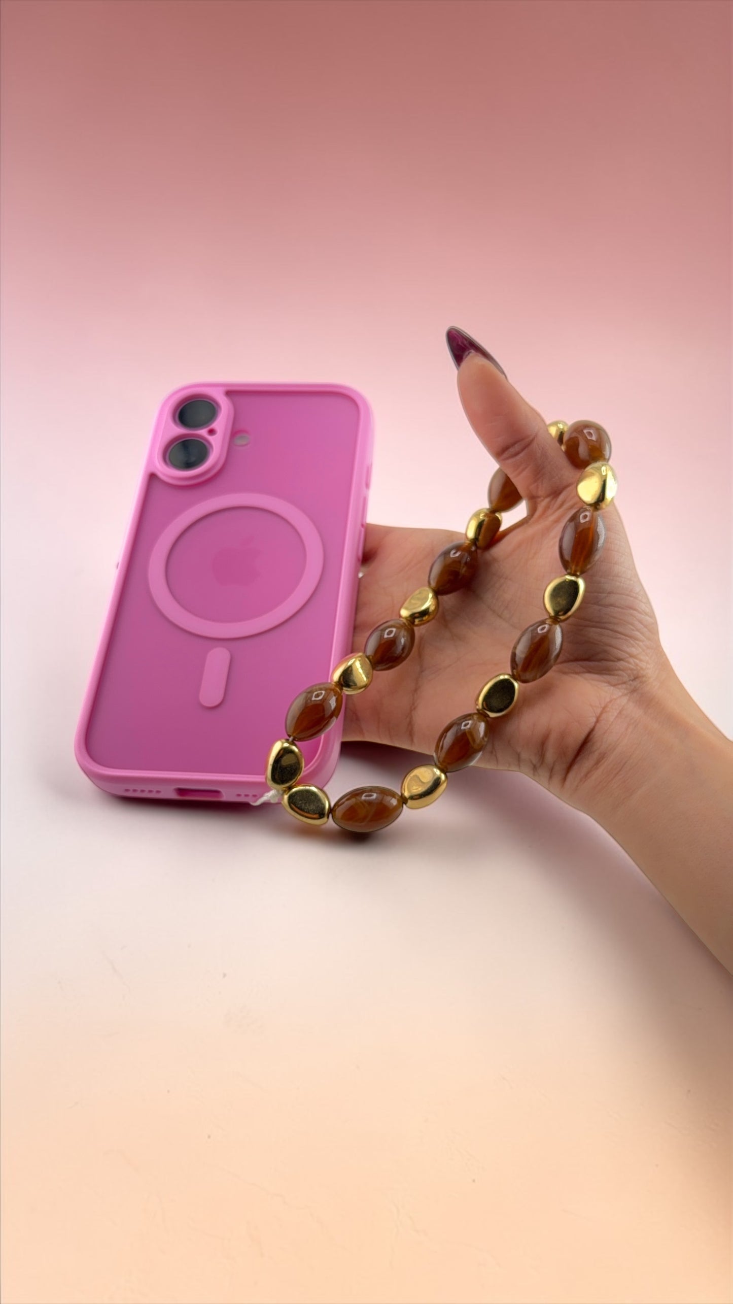 Hand holding a pink phone case with a gold chain against a gradient background