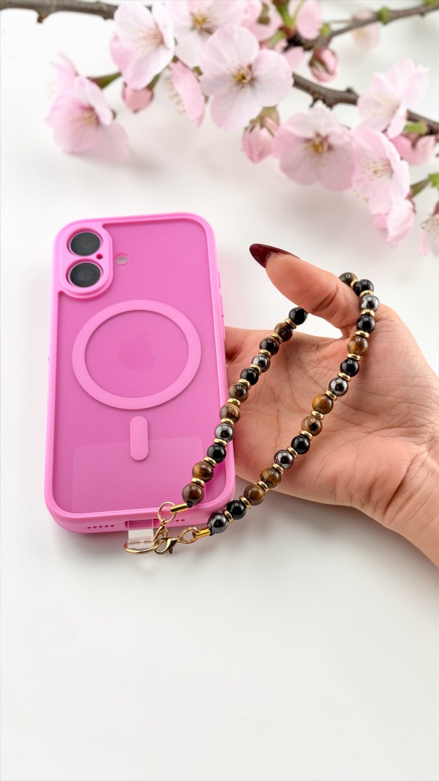 Pink phone case with a chain holder held by a hand with cherry blossoms in the background