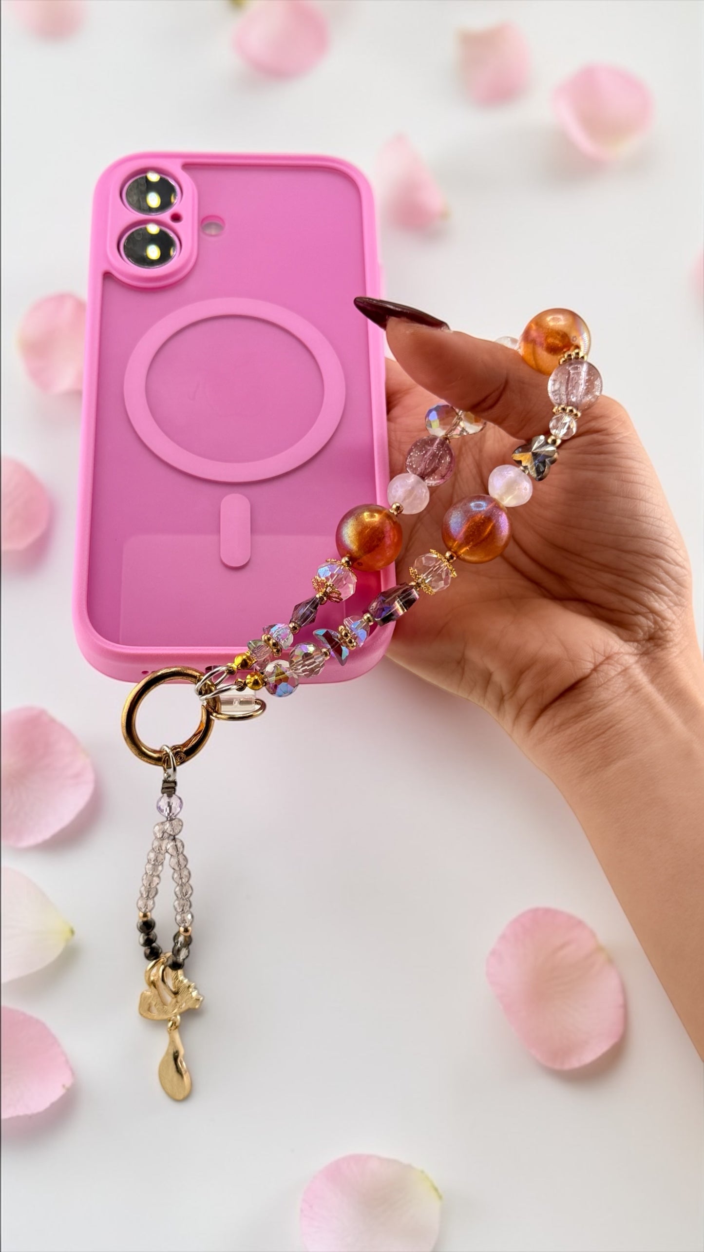 Pink phone case with a colorful beaded charm held by a hand on a light background.