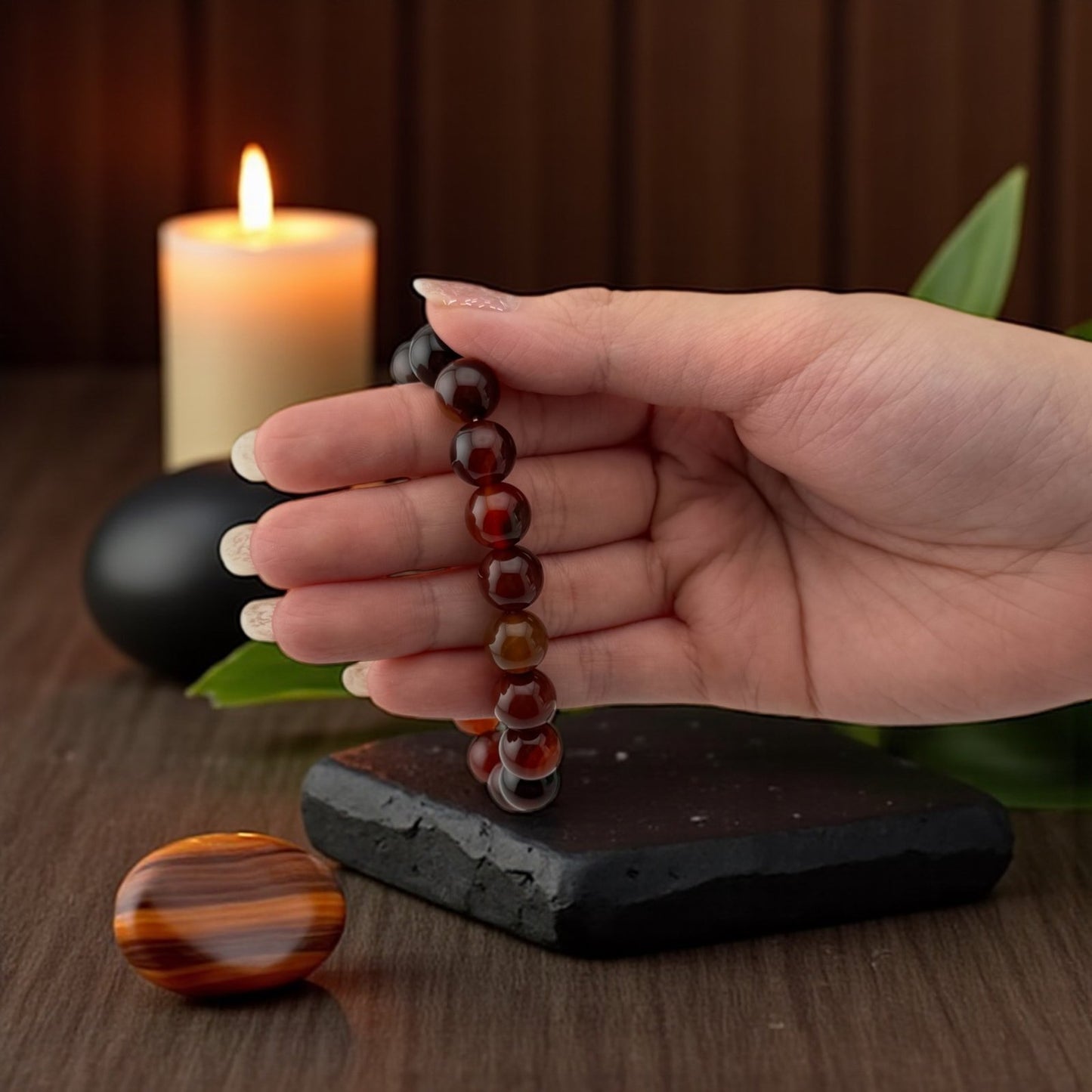 Hand holding a beaded necklace with a candle and stone in the background