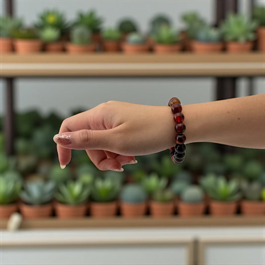 Hand wearing a red beaded bracelet with a blurred background of plants