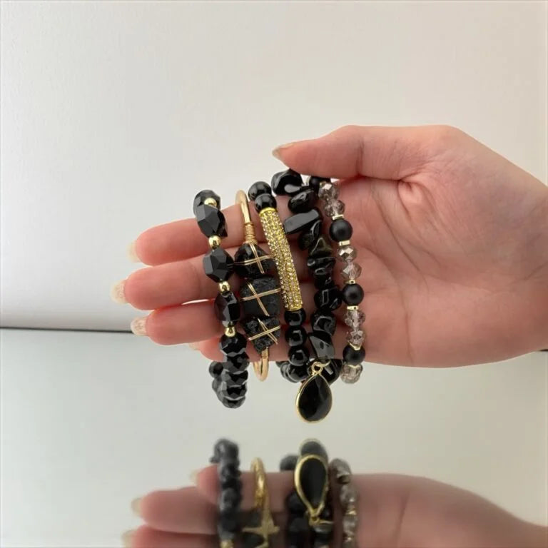 Hand holding a stack of black and gold beaded bracelets against a white background