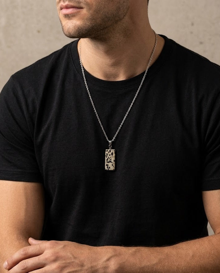 Man wearing a black t-shirt and a necklace with a pendant against a neutral background