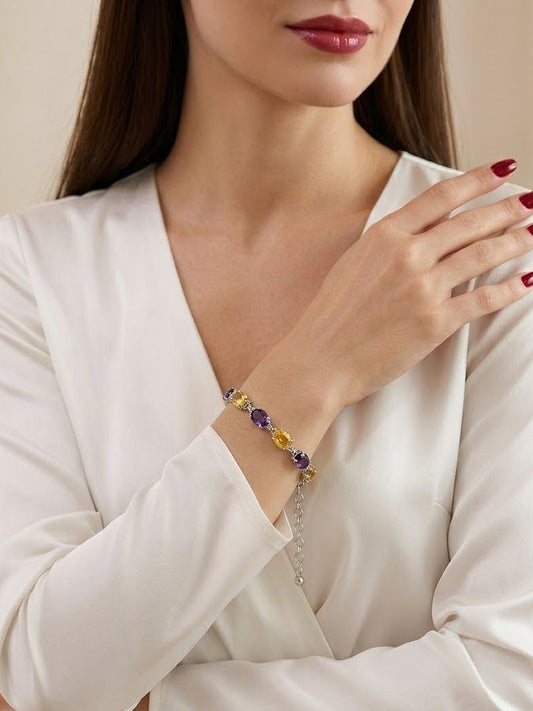 A close-up of a woman wearing a delicate beaded bracelet on her wrist. The bracelet features small purple and yellow beads with a silver-toned chain extender.