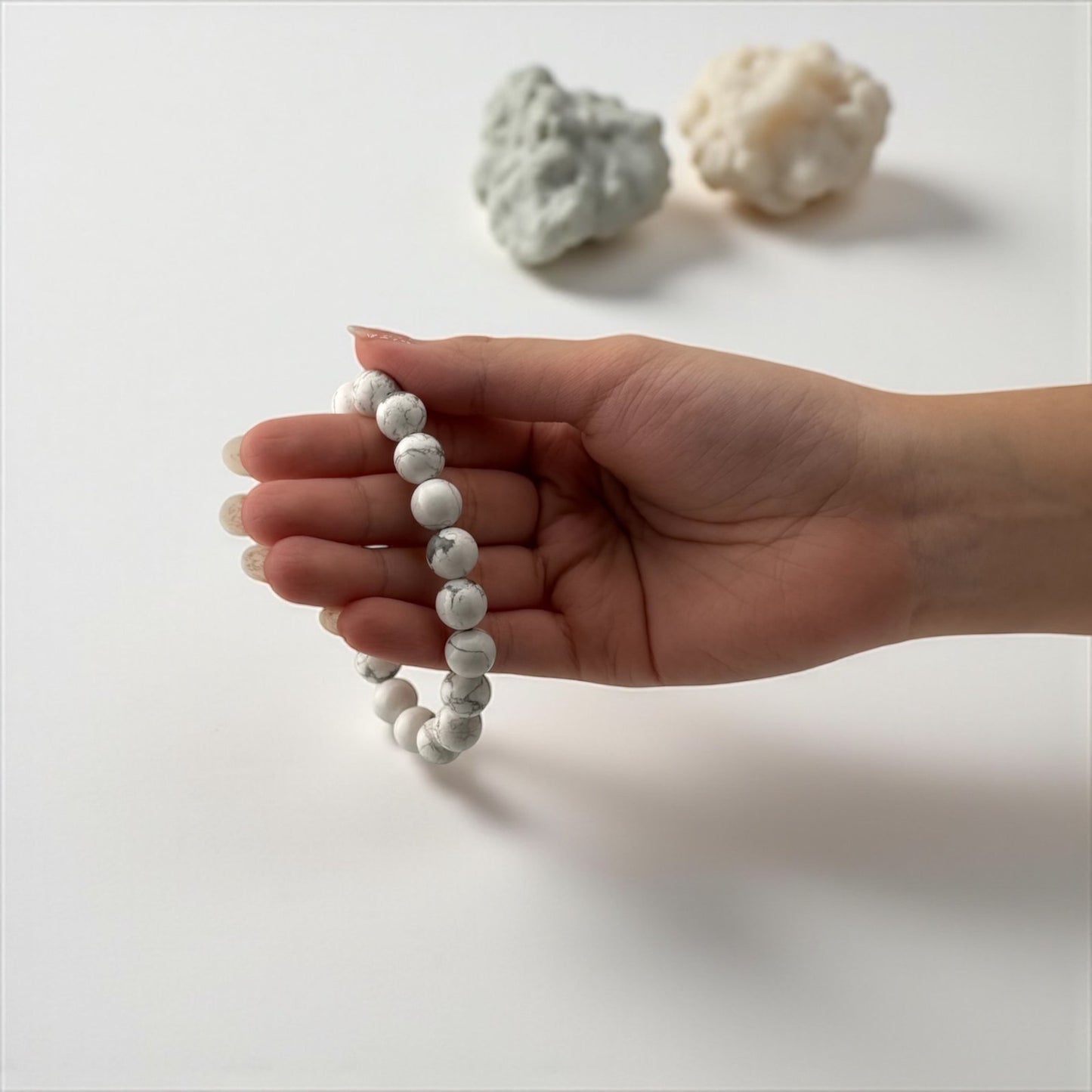 Hand holding a white beaded bracelet with two pieces of white coral on a light background