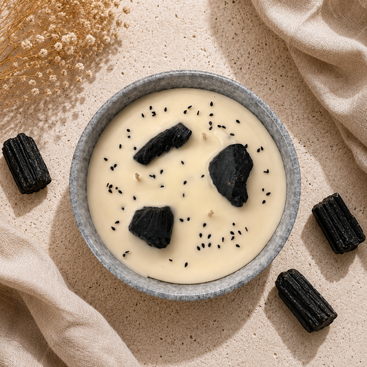 Bowl of creamy dessert with black sesame seeds and dark chocolate pieces on a beige surface.