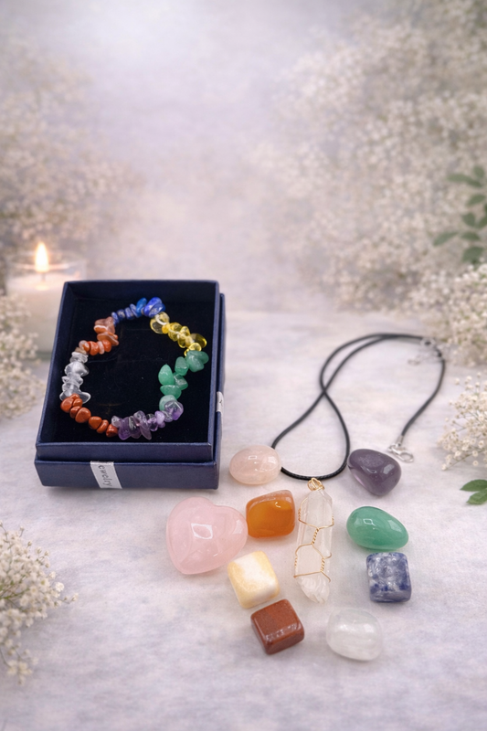 Set of colorful crystal necklaces and bracelets on a soft surface with a blurred floral background.