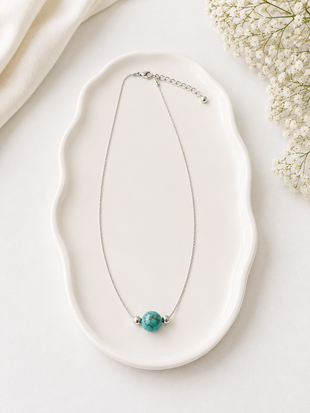 Necklace with a turquoise bead on a white dish with flowers in the background