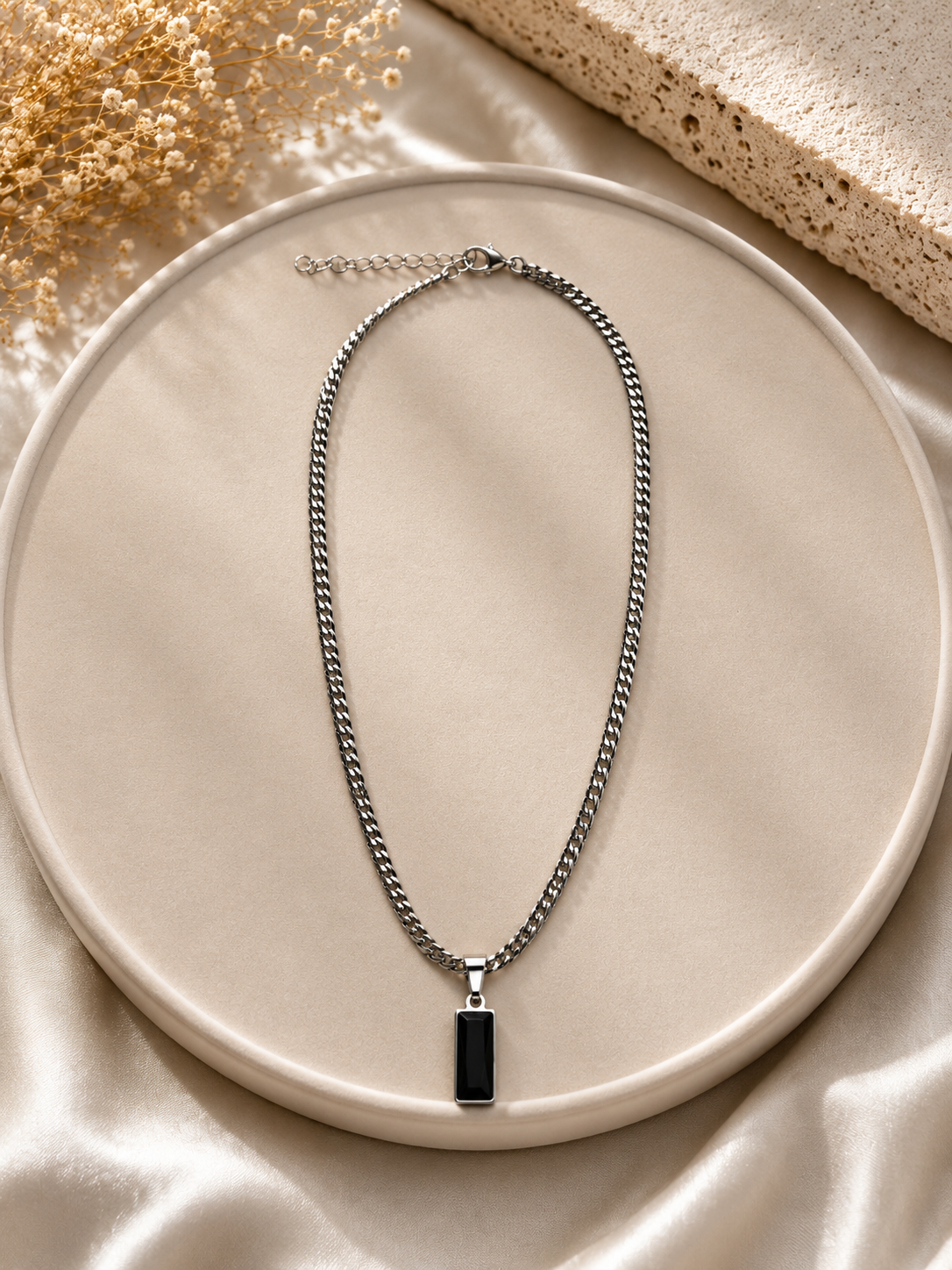 Silver chain necklace with a black pendant on a beige plate
