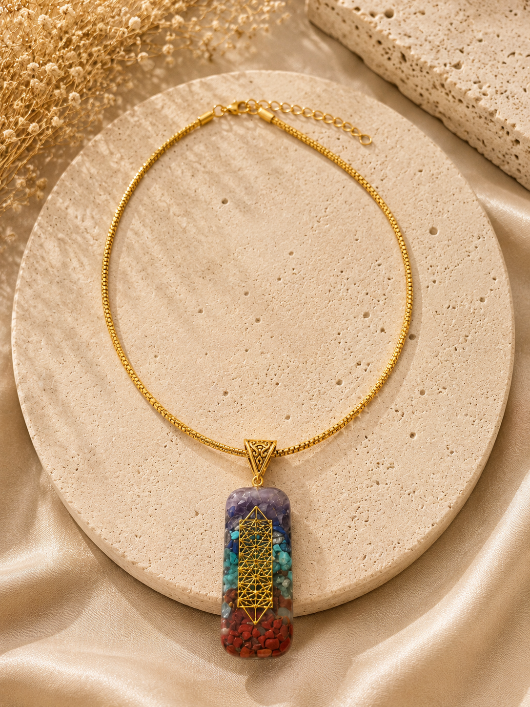 Gold necklace with a colorful pendant on a beige stone surface