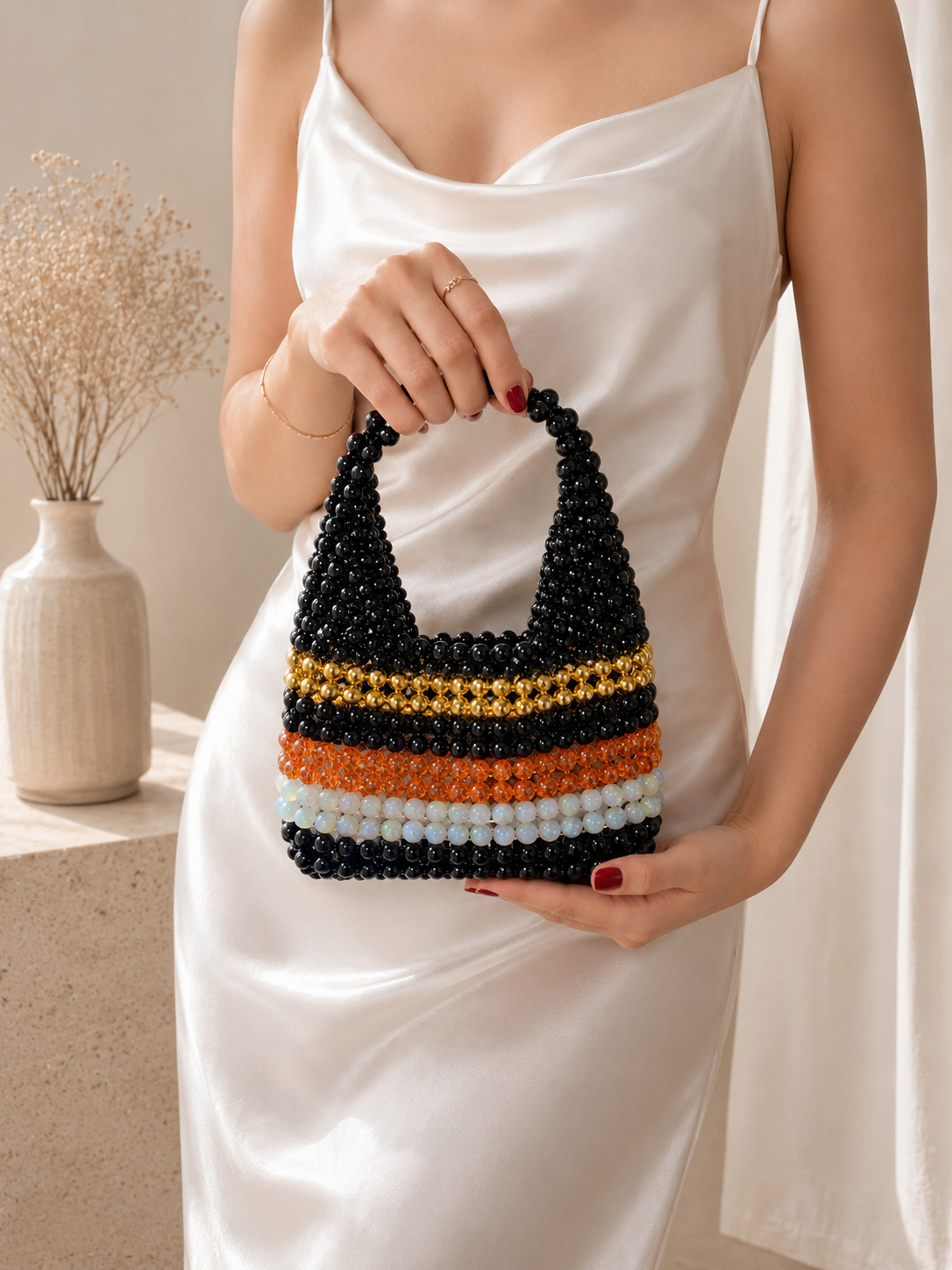 Person holding a beaded handbag with black, orange, and white stripes in a minimalistic setting.