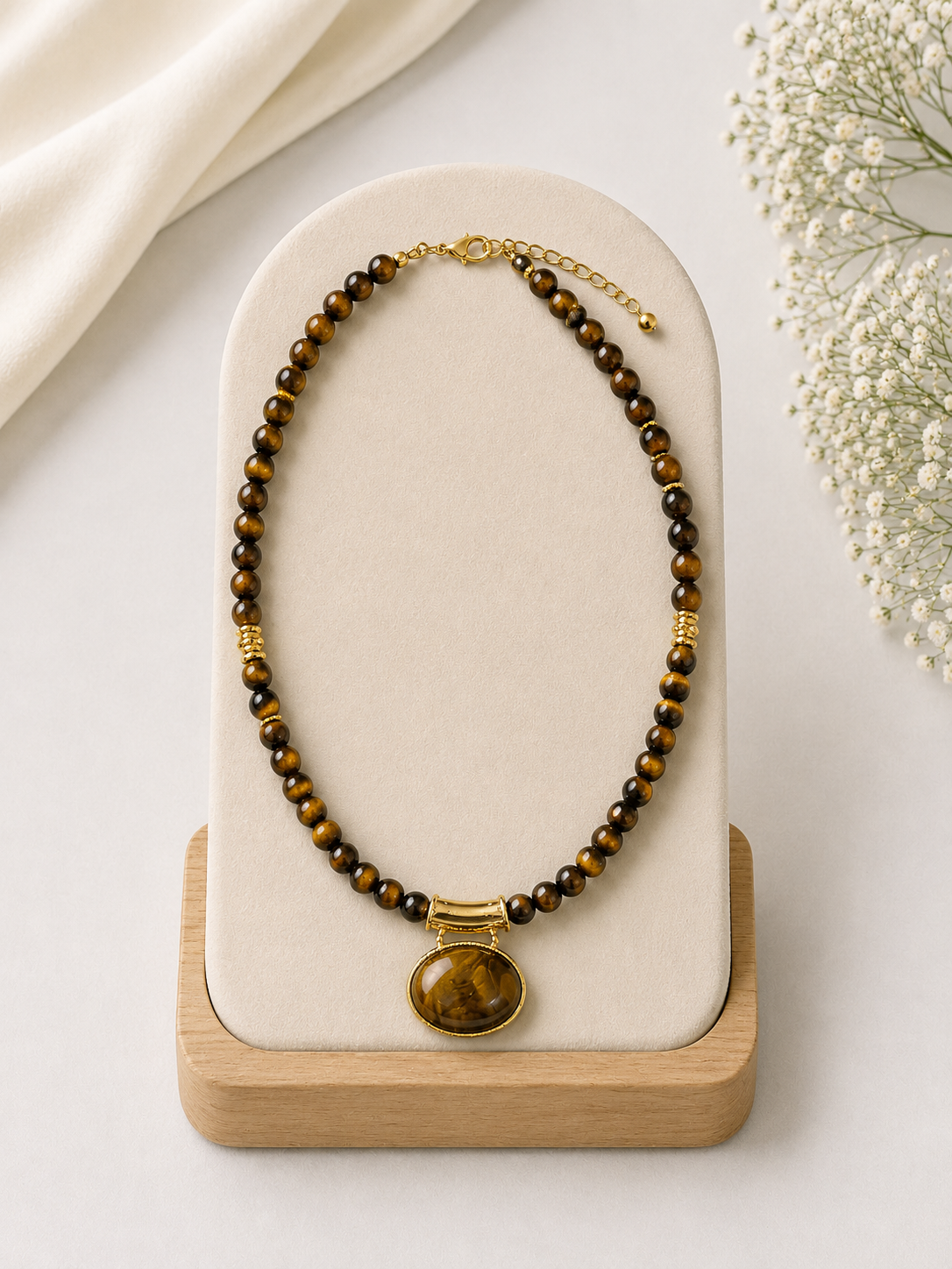 Necklace with brown beads and a gold pendant on a white stand with a light background