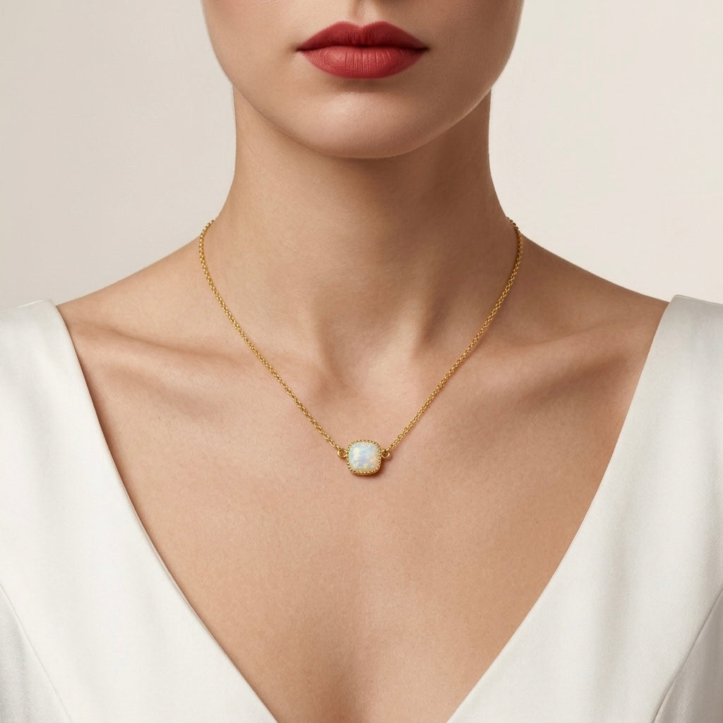 Gold necklace with a pendant worn by a person in a white top against a neutral background