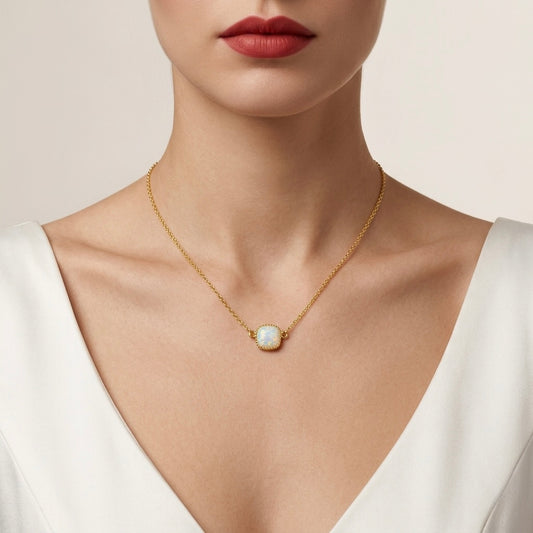 Gold necklace with a pendant worn by a person in a white top against a neutral background