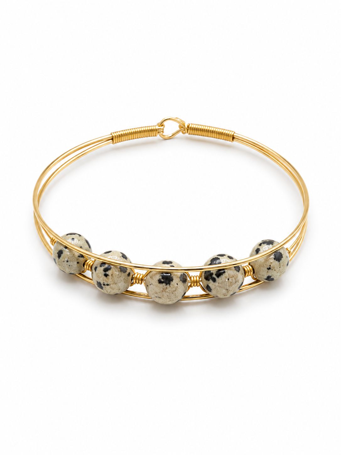A gold wire bangle bracelet featuring five round, speckled Dalmatian stone beads spaced along the front, set against a plain white background.