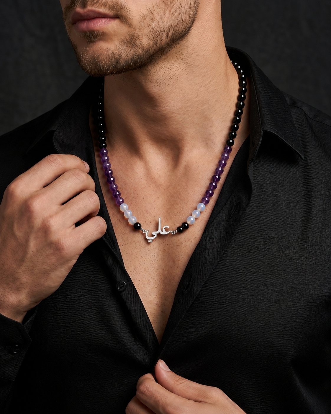 Man wearing a beaded necklace with a dark shirt against a black background