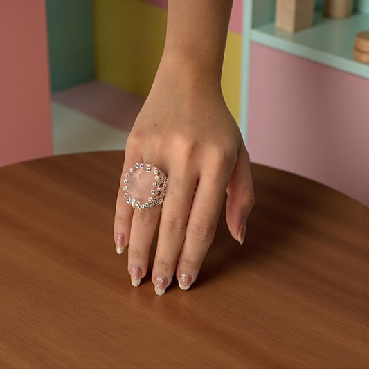 Hand wearing a ring on a wooden surface with a colorful background