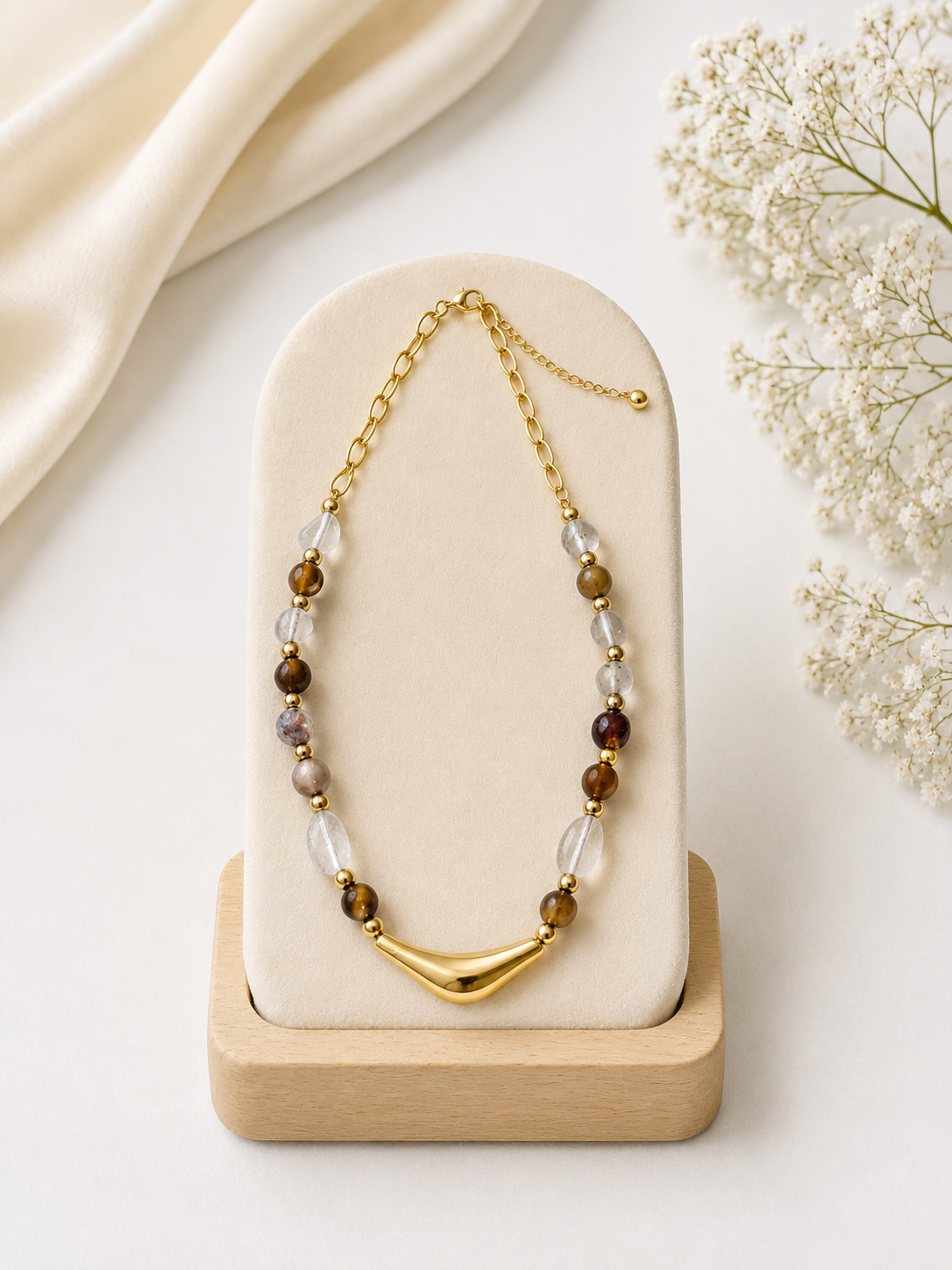 Necklace with beads and gold chain on a wooden stand with flowers in the background