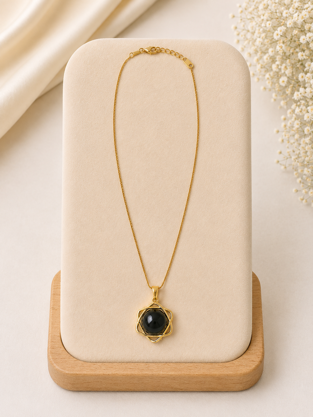 Gold necklace with a black pendant on a beige stand with a light background