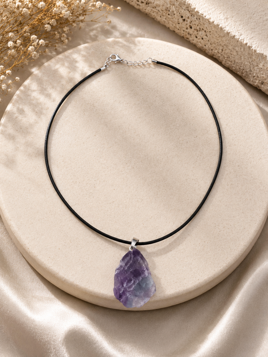Necklace with a purple teardrop pendant on a beige surface