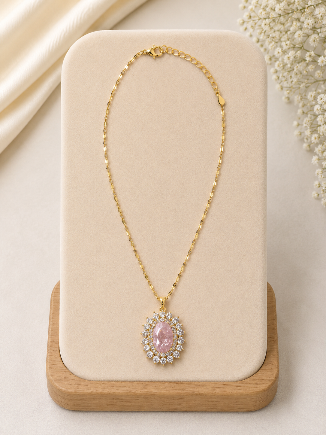Gold necklace with a pink gemstone on a beige display stand.