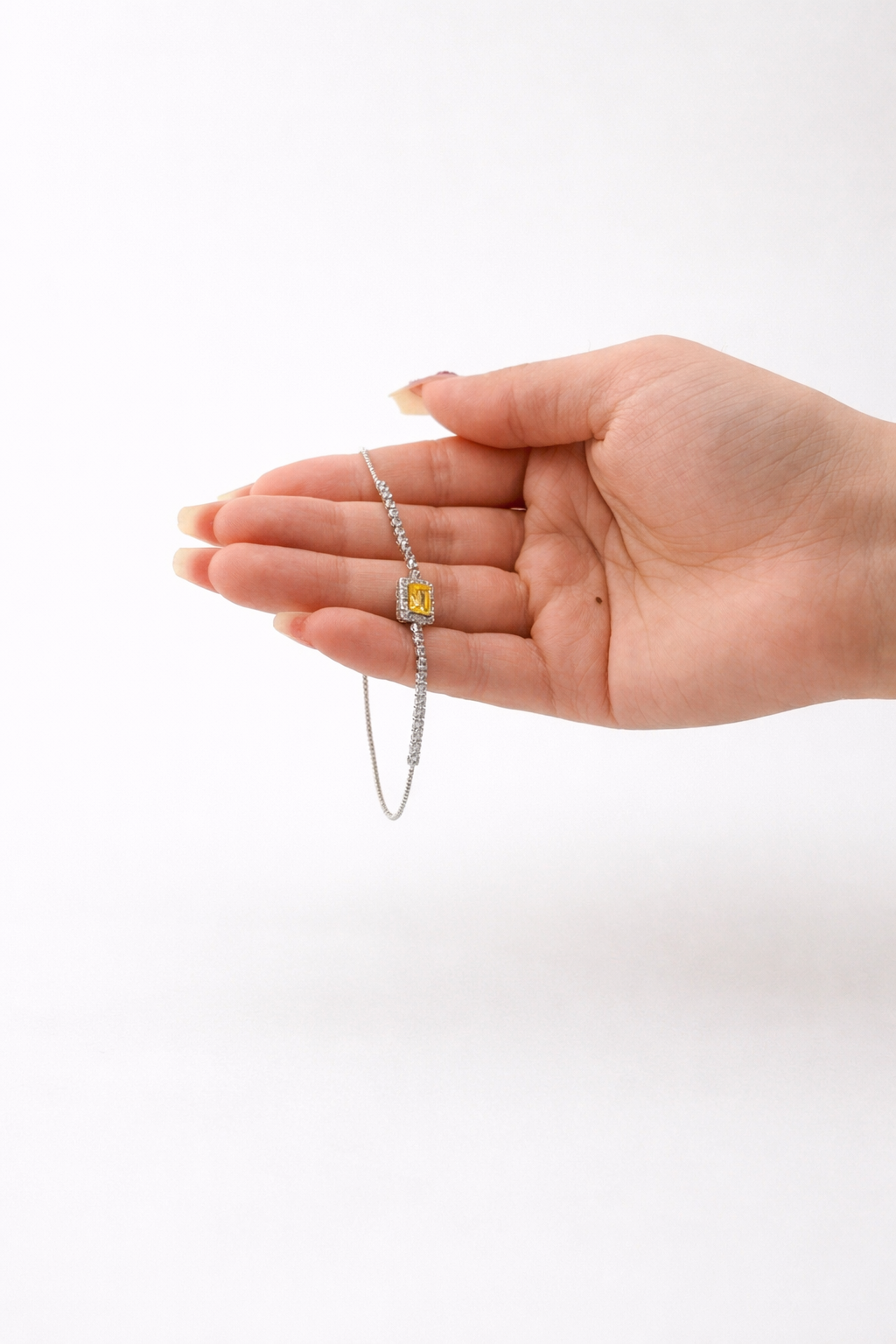 Hand holding a silver bracelet with a yellow gemstone on a white background