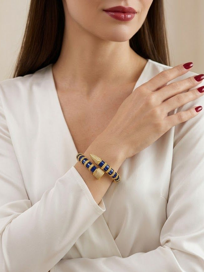 A close-up of a woman wearing a double beaded bracelet with navy blue and gold beads, paired with a white long-sleeve blouse.