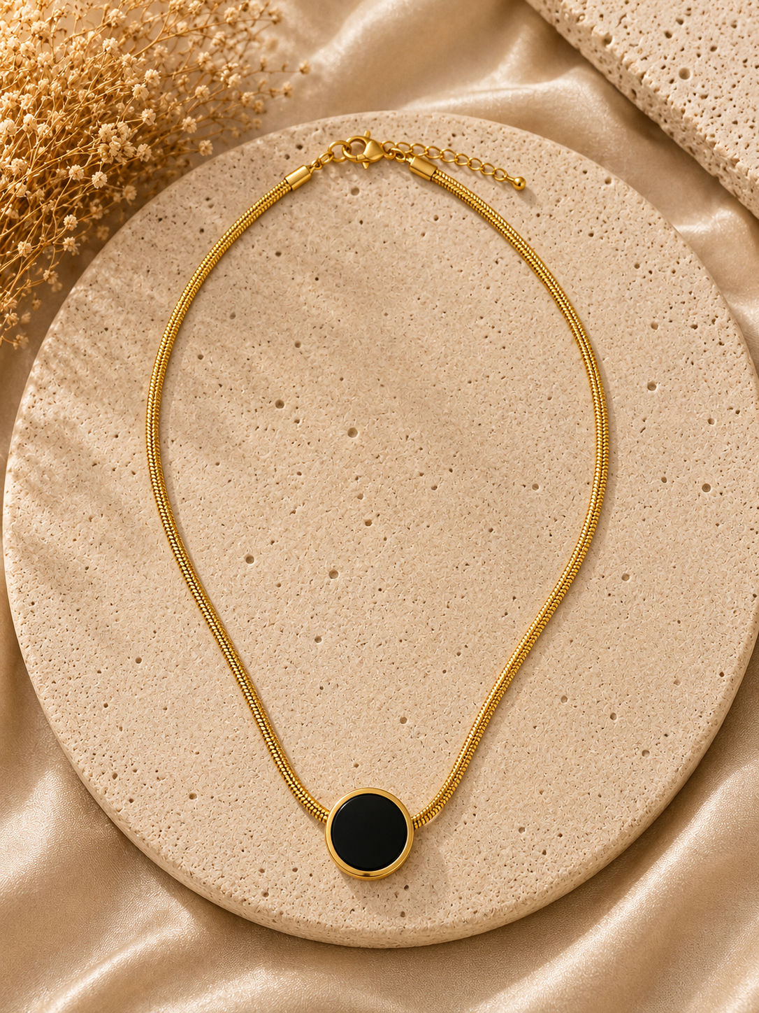 Gold necklace with a black pendant on a beige surface