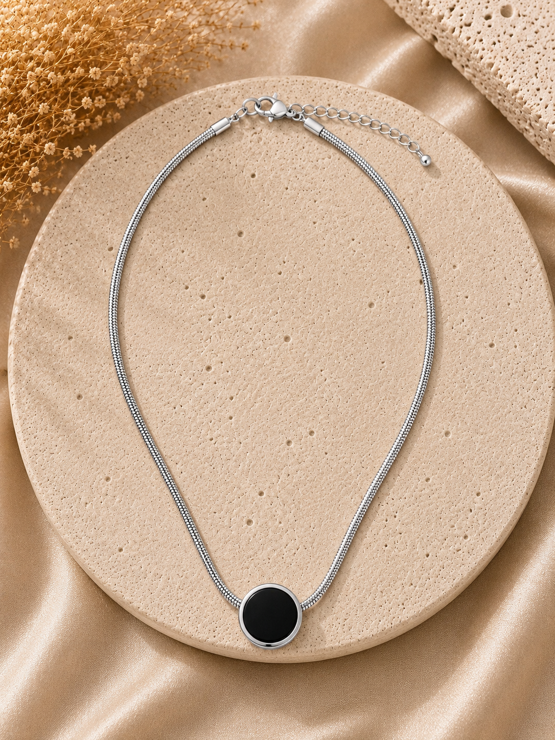 Silver necklace with a black pendant on a beige stone surface