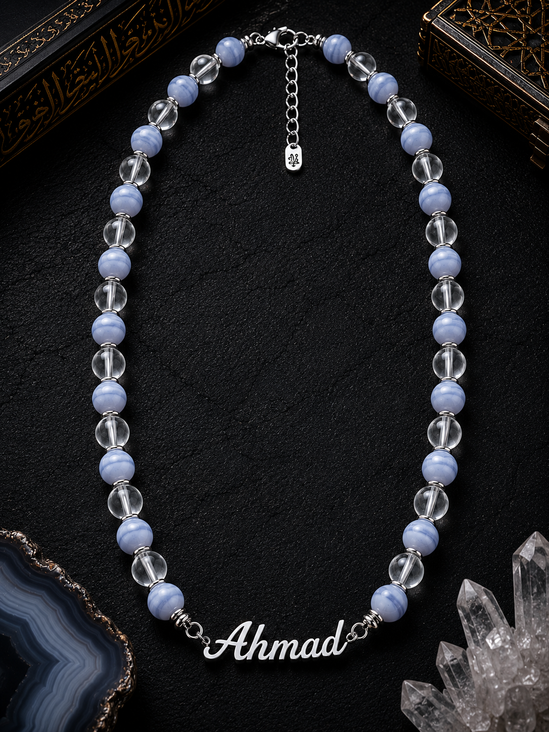 Necklace with blue and clear beads and a nameplate on a dark surface
