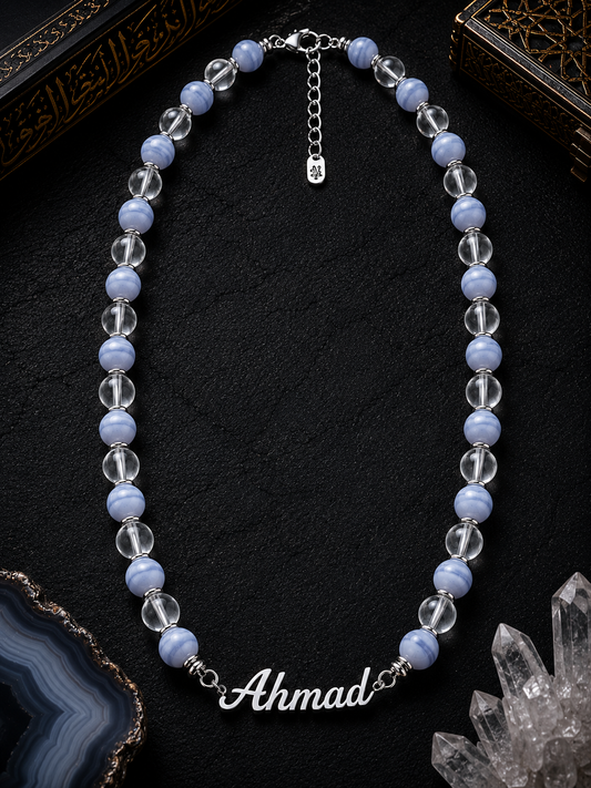 Necklace with blue and clear beads and a nameplate on a dark surface