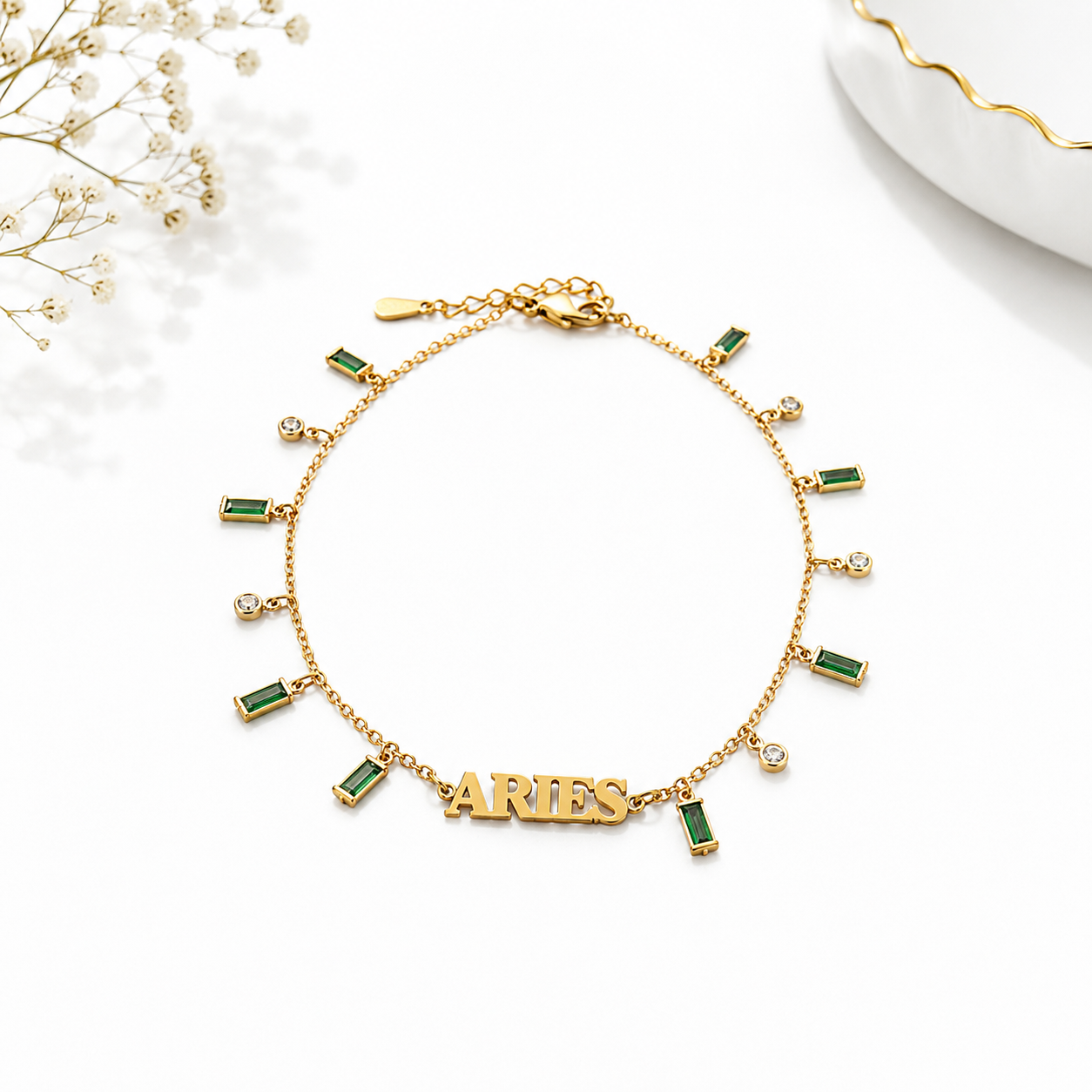 Gold bracelet with 'ARIES' charm and green gemstones on a white background