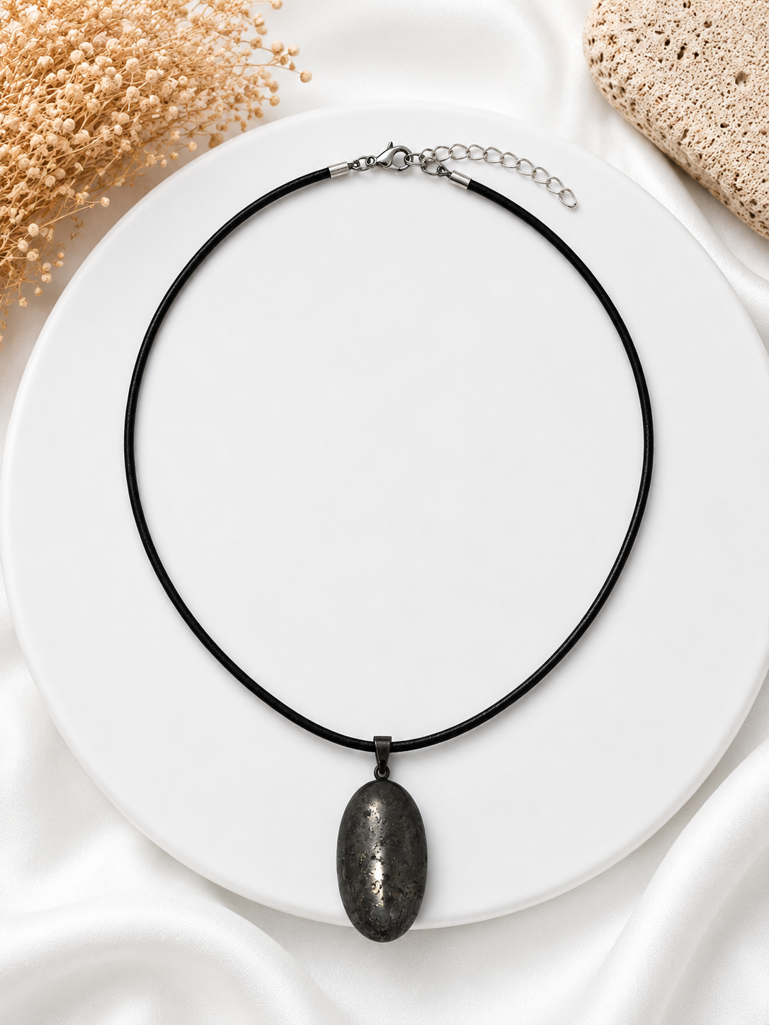 Necklace with a black cord and pendant on a white plate with beige flowers and stones.