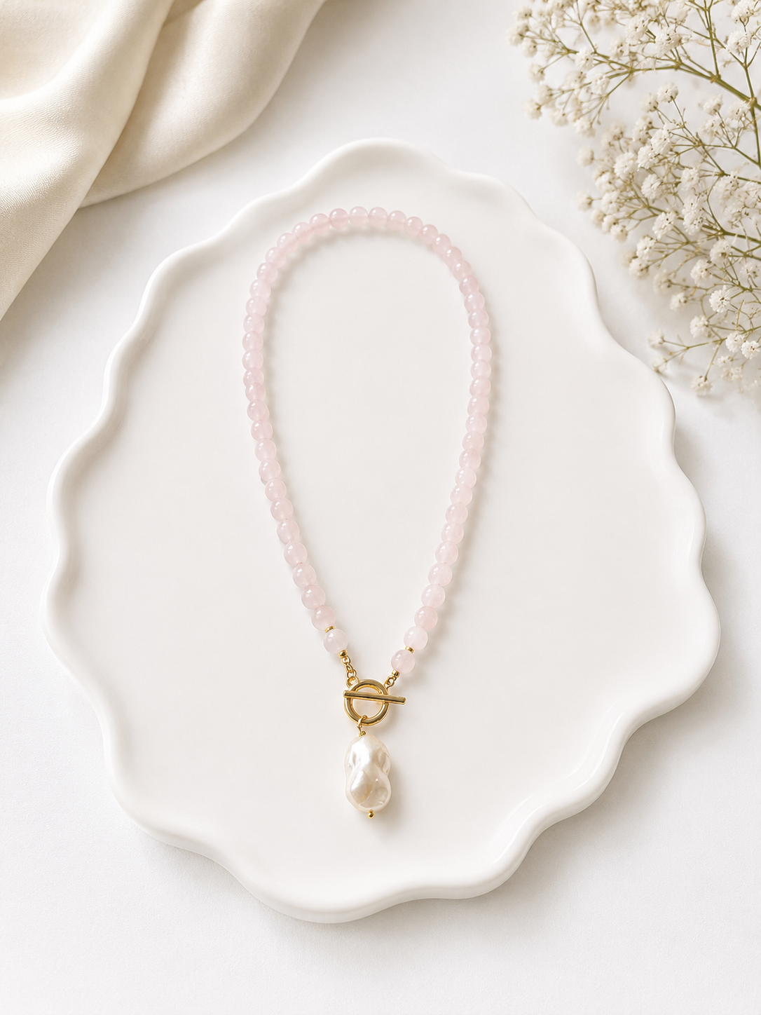 Necklace with pink beads and a gold clasp on a white dish with flowers in the background